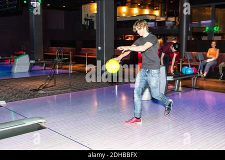 Die ganze Länge des Teenagers hält Ball auf Parkettboden Gegen Freunde auf der Bowlingbahn Stockfoto