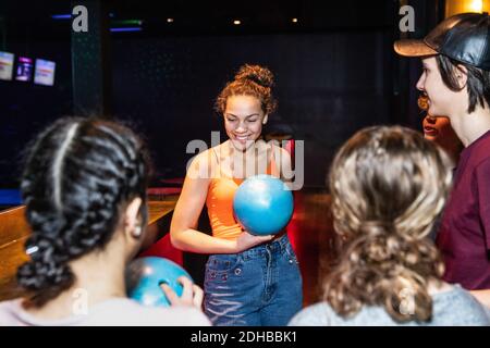 Lächelndes Teenager-Mädchen hält Bowling-Ball, während unter Freunden stehen Stockfoto