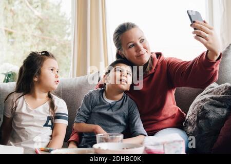 Tochter, die Mutter anschaut, während sie Selfie mit autistischem Bruder nimmt Beim Vater im Wohnzimmer sitzen Stockfoto