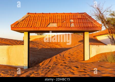 Mauer und gefliestes Tor in Sanddünen in der Wüste in Al Madam Geisterdorf, Vereinigte Arabische Emirate begraben, Sonnenuntergang. Stockfoto