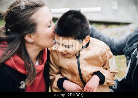 Mutter küsst behinderten Sohn auf Rollstuhl im Hof sitzen Stockfoto
