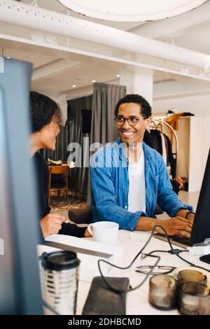 Lächelnde männliche und weibliche Kollegen, die sich unterhalten, während sie am Schreibtisch sitzen Im Büro Stockfoto