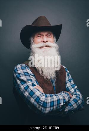 Porträt eines glücklichen älteren Mannes mit Cowboyhut gegen Grau Hintergrund Stockfoto