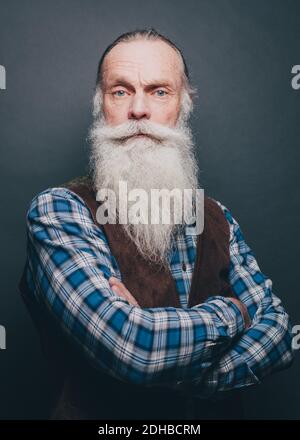 Porträt eines selbstbewussten bärtigen älteren Mannes, der die Arme überkreuzt Grauer Hintergrund Stockfoto