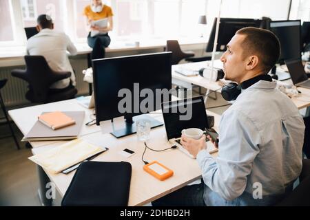 Männlicher Computerprogrammierer, der weg schaut, während er am Schreibtisch innen sitzt Kreatives Büro Stockfoto