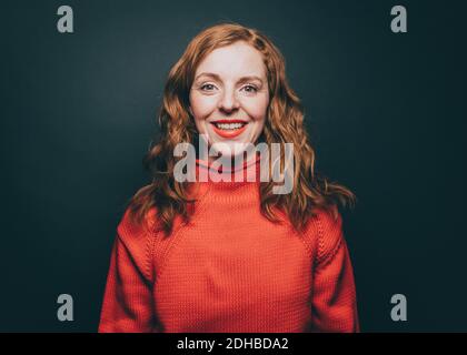 Porträt einer lächelnden Frau in orange oben auf grauem Hintergrund Stockfoto