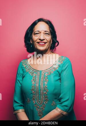 Porträt einer lächelnden älteren Frau, die Salwar Kameez gegen Rosa trägt Hintergrund Stockfoto