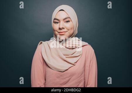 Porträt einer lächelnden jungen Frau mit Hijab vor grauem Hintergrund Stockfoto