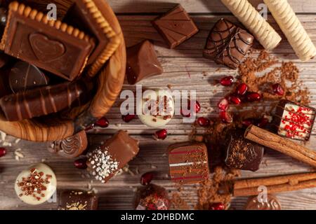 Eine Schüssel mit verschiedenen Pralinen und Schokoladenkekse auf Holzhintergrund mit Kakaopulver Zimtschnecken, Pirouetten und Kokosnussstreuseln schaffen Stockfoto