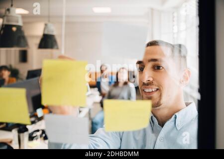 Männlicher Computerprogrammierer klebende Notiz auf Glas während der Sitzung kleben Mit Kollegen im Kreativbüro Stockfoto