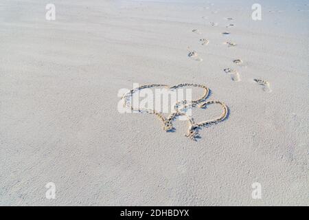 Herz Symbol auf einem Sand des Strandes mit weicher blauer Welle auf dem Hintergrund. Ein Herzsymbol auf einem Sandstrand mit Schaum und Wasser Hintergrund geschrieben. Valentinstag Stockfoto