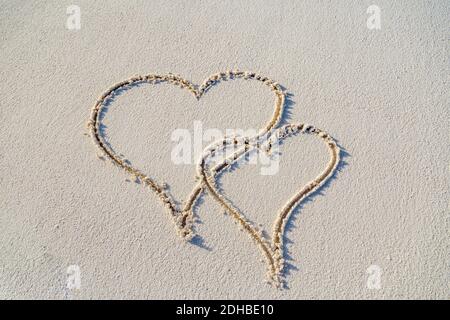 Herz Symbol auf einem Sand des Strandes mit weicher blauer Welle auf dem Hintergrund. Ein Herzsymbol auf einem Sandstrand mit Schaum und Wasser Hintergrund geschrieben. Valentinstag Stockfoto