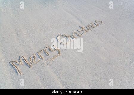 Frohe Weihnachten handgeschrieben in Sand am Strand. Winterurlaub Konzept, Natursand sonnigen Tag, kopieren Raum für Text Stockfoto