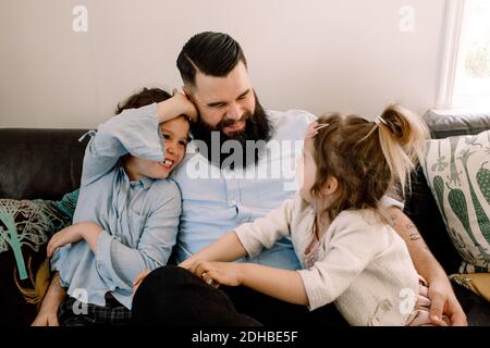 Glücklicher Vater spielt mit fröhlichen Töchtern, während er auf dem Sofa sitzt Zu Hause Stockfoto