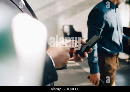 Mittelteil des Geschäftsmannes, der das Handy benutzt, während er Tee trint Büro Stockfoto