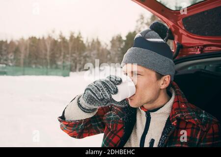 Im Winter trinkender Mann im Kofferraum auf dem Parkplatz Stockfoto