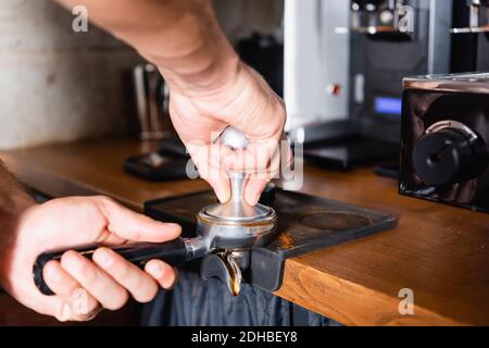 Beschnittene Ansicht des Barista, der gemahlenen Kaffee in einem Portafilter presst Stockfoto