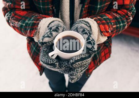 Mittelteil des Mannes, der die Kaffeetasse hält, während er auf Schnee steht Stockfoto