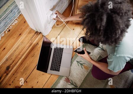 High-Angle-Ansicht der jungen Frau stecken Handy-Ladegerät In der Steckdose zu Hause Stockfoto