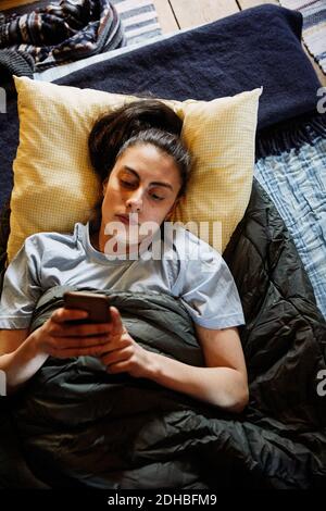 High-Winkel-Ansicht der jungen Frau mit Smartphone, während Liegen auf Matratze in der Hütte Stockfoto