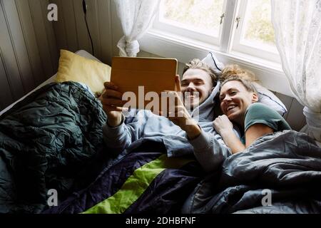 High-Angle-Ansicht von lächelnden Freunden, die Filme über digitale Medien ansehen Tablet, während Sie im Cottage auf dem Bett liegen Stockfoto