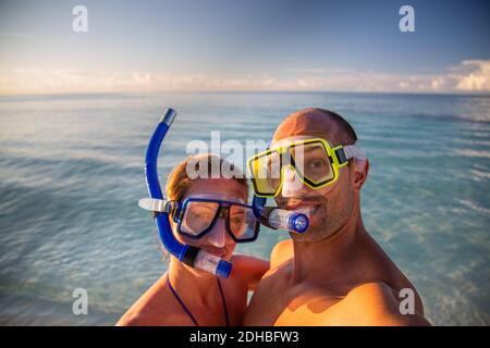 Paar in Masken am Strand mit Meereshorizont. Sonnige Sommerferien Reise lustig Selfie. Nettes Paar Porträt, zusammen Stockfoto