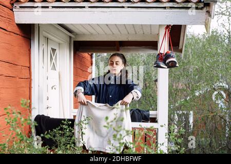 Junge Frau trocknet Kleidung, während sie vor der Hütte steht Stockfoto