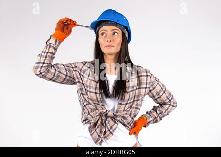 Weibliche Mechanikerin trägt blauen Hut hält einen Schraubenschlüssel und schaut nachdenklich zur Seite. Weißer Hintergrund. Stockfoto