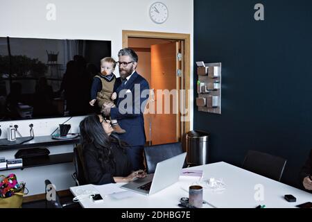 Lächelnde Geschäftsfrau suchen männlichen Kollegen mit Sohn im Büro stehen Stockfoto
