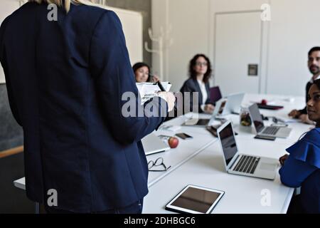 Mittelteil der Geschäftsfrau, die Dokument hält, während sie mit Kollegen spricht Meeting im Sitzungssaal Stockfoto