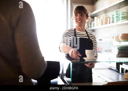 Lächelnde Barista, die männlichen Gästen im Café Kaffee serviert Stockfoto