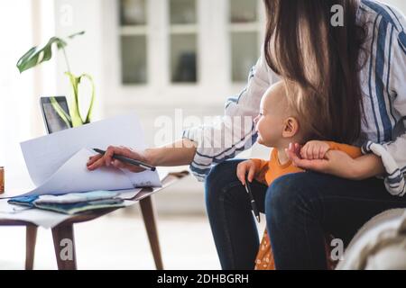 Mittelteil der arbeitenden Mutter, die Dokumente mit Baby-Mädchen bei prüft Heimbüro Stockfoto