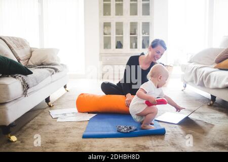 Lächelnde Mutter, die während des Übens auf die Tochter zeigt, die auf den Laptop zeigt Yoga im Wohnzimmer Stockfoto