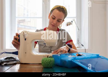 Junge Schneiderin mit Nähmaschine, während sie gegen das Fenster sitzt Zu Hause Stockfoto