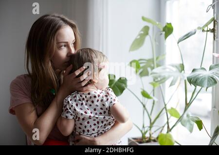 Mutter küsst Tochter beim Blick durch Fenster zu Hause Stockfoto