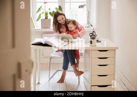 Buchhalterin sitzt mit Tochter während der Arbeit auf Laptop an Zu Hause Stockfoto