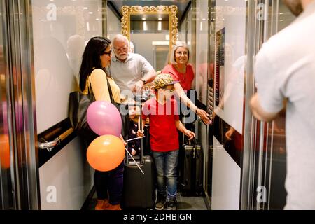 Frau, die im Aufzug den Knopf drückt, während sie mit der Familie steht Stockfoto