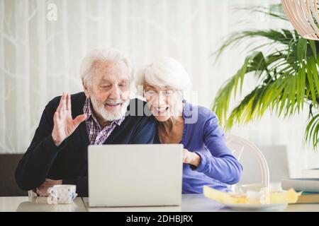 Fröhliche ältere Paar Videoanrufe durch Laptop am Tisch in Pflegeheim Stockfoto