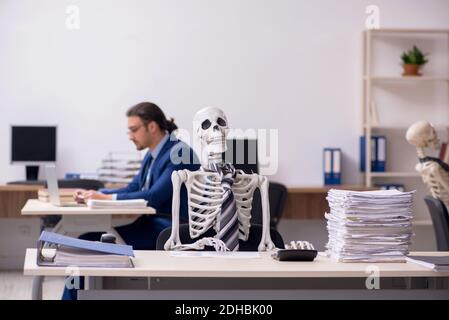 Junger männlicher Angestellter mit Skeletten im Büro Stockfoto