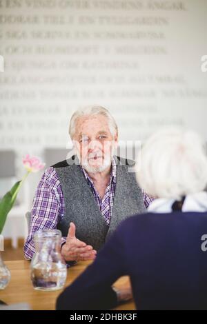 Älterer Mann, der mit einer Frau spricht, während er am Tisch sitzt Pflegeheim Stockfoto