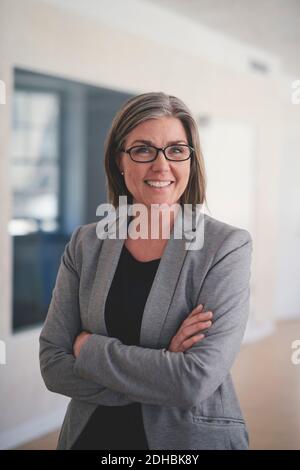 Porträt einer selbstbewussten reifen Geschäftsfrau stehend mit gekreuzten Armen Büro Stockfoto