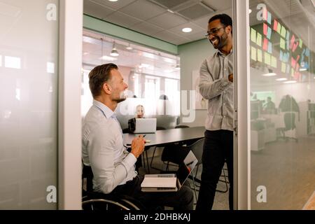 Lächelnder Geschäftsmann, der einen behinderten Kollegen im Rollstuhl ansieht Konferenzraum Stockfoto