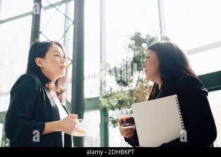 Geschäftsfrauen, die Kaffee trinken, während sie in einem hell erleuchteten Büro diskutieren Stockfoto