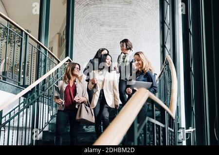 Low-Angle-Ansicht der lächelnden Unternehmerinnen, die sich nach unten bewegen Treppe im Büro Stockfoto