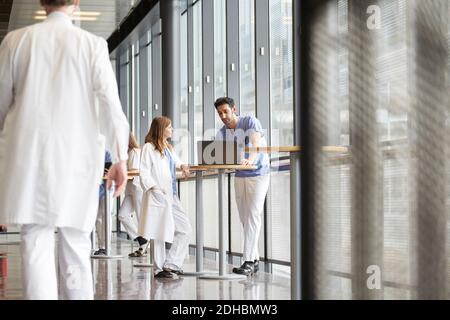 Mittelteil des Arztes beim Gehen, während die Mitarbeiter des Gesundheitswesens über den Laptop diskutieren Im Flur im Krankenhaus Stockfoto