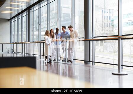 In voller Länge medizinisches Personal diskutieren über Laptop auf Tisch in Korridor gegen Fenster im Krankenhaus Stockfoto