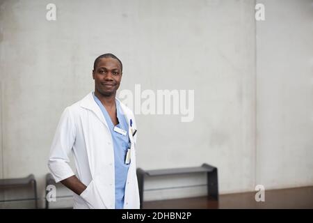 Portrait von zuversichtlich männlichen Arzt stehen mit Händen in den Taschen Gegen die Wand im Krankenhaus Stockfoto