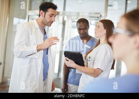 Selbstbewusste, multiethnische Krankenschwestern und Ärzte diskutieren über digitale Tablets in Lobby im Krankenhaus Stockfoto