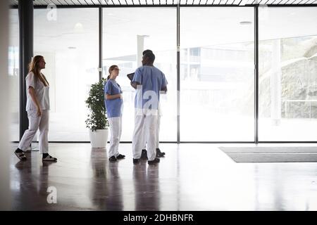 Volle Länge der Ärzte und Krankenschwestern diskutieren, während im Stehen Korridor gegen Fenster im Krankenhaus Stockfoto