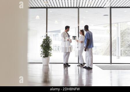 Die ganze Länge der Krankenschwestern und Arzt über digitale Tablette diskutieren Gegen das Fenster im Flur im Krankenhaus Stockfoto